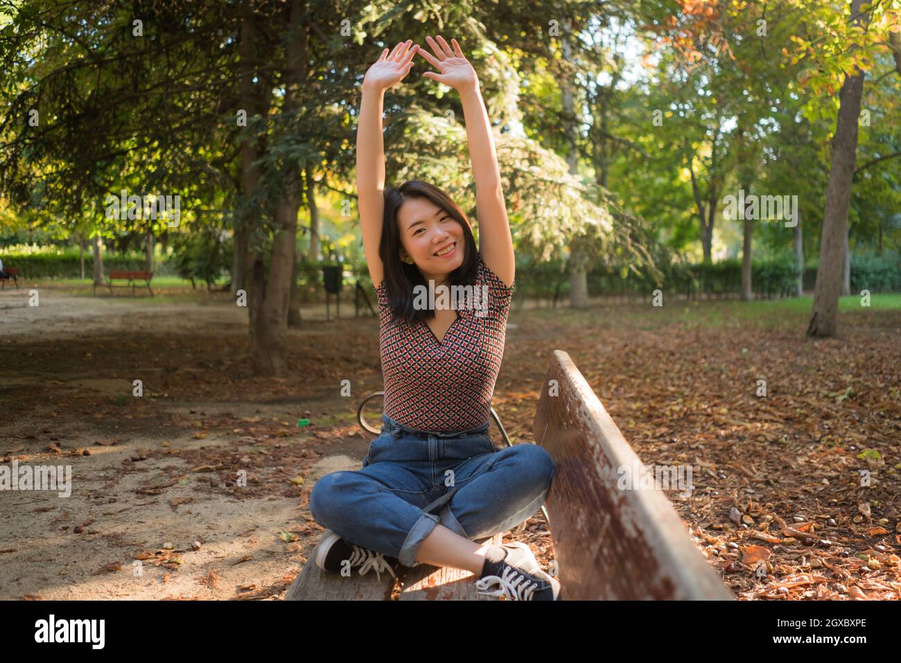 outdoors lifestyle portrait of young happy and beautiful Asian Korean woman enjoying relaxed and cheerful at sitting on city park bench in Autumn Stock Photo
