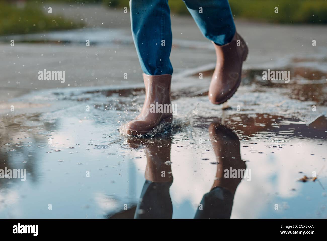 Woman wearing rain rubber boots walking running and jumping into puddle with water splash and drops in autumn rain. Stock Photo