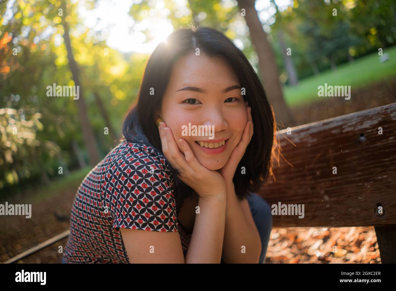 outdoors lifestyle portrait of young happy and beautiful Asian Korean woman enjoying relaxed and cheerful at sitting on city park bench in Autumn smil Stock Photo