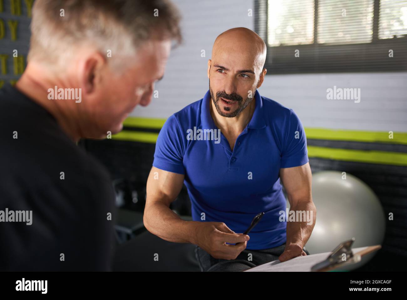 Male physio therapist and wellness personal trainer having a consultation with elderly senior man on strength and rehabilitation and assisted exercise Stock Photo