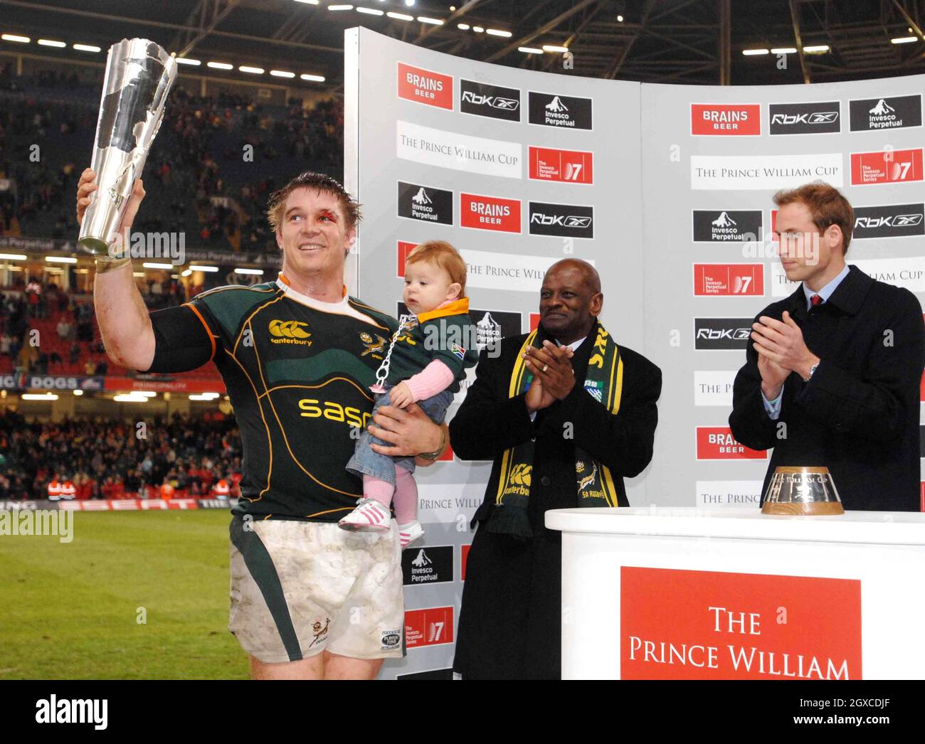 South Africa's rugby team captain John Smit holds his daughter Emma after collecting the Prince William Cup from Prince William, as chairman of the SA Rugby Union Mpumeleo Tshume looks on, following South Africa winning the inaugural Wales v South Africa Prince William Cup match at the Millennium Stadium, Cardiff on November 24, 2007. Stock Photo