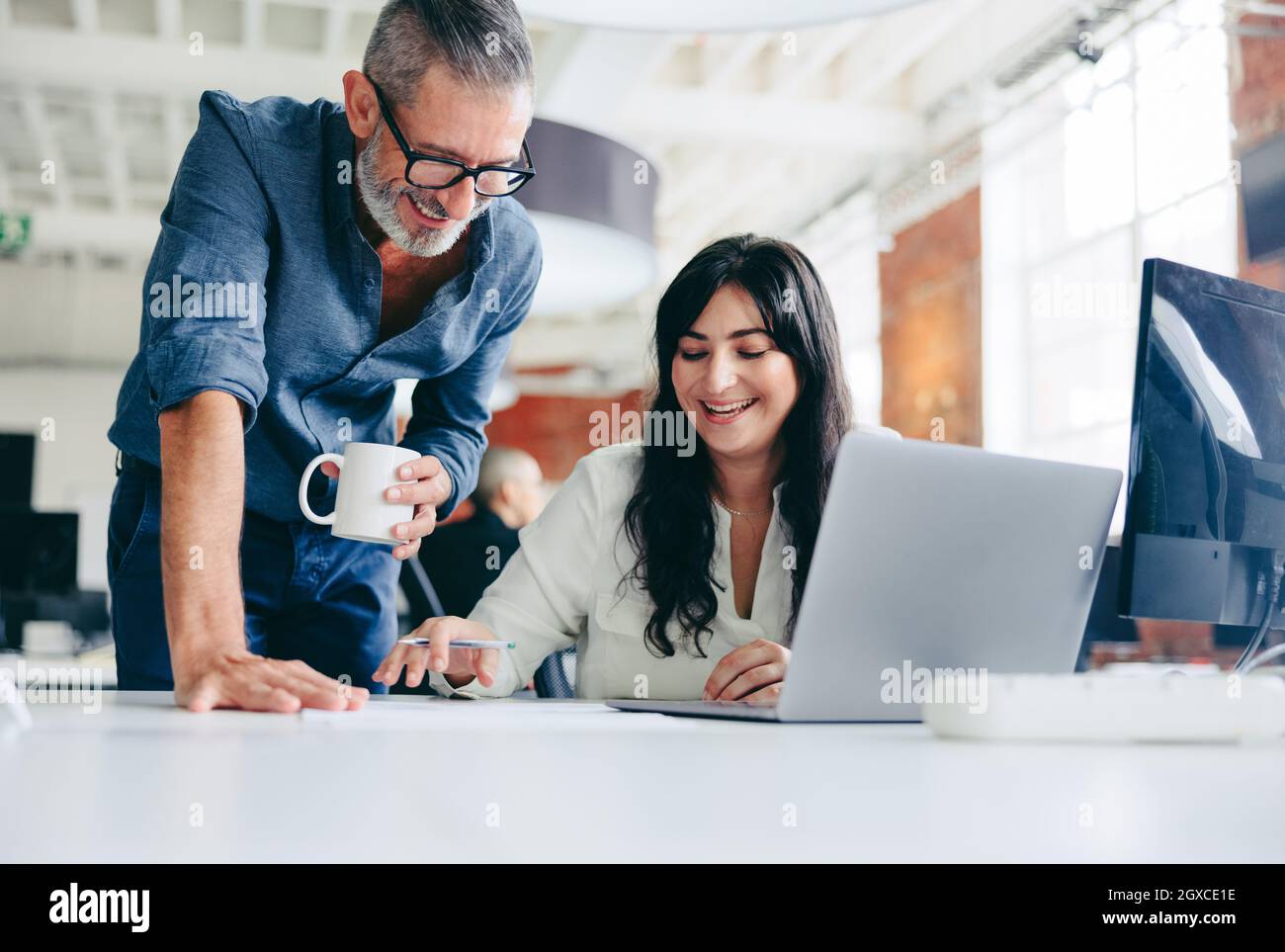 Two happy colleagues collaborating on a new project in the office. Mature businessman teaming up with his female colleague in a modern office. Two col Stock Photo