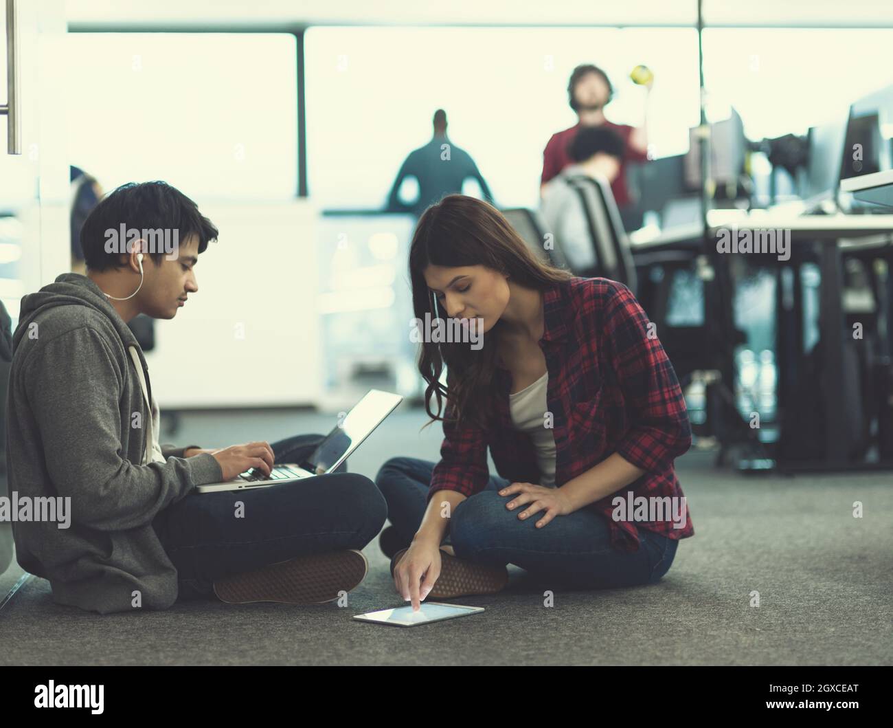 young software developers couple using laptop and tablet computer writing programming code while sitting on the floor at modern creative startup offic Stock Photo