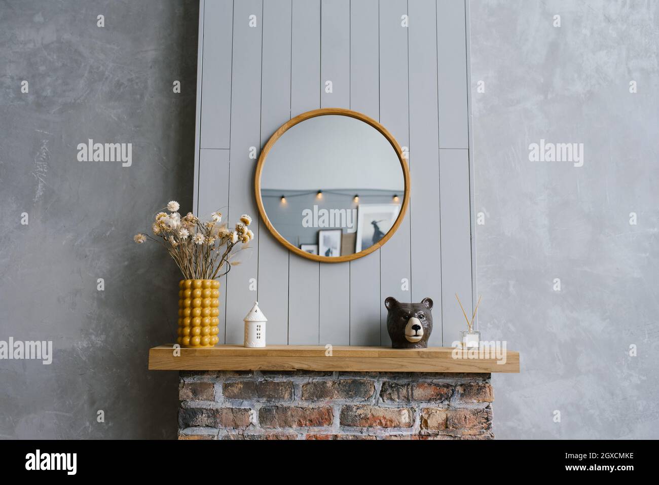Stylish Scandinavian minimalistic interior. Modern interior of a country house in gray and yellow colors.  Round mirror over the brick fireplace in th Stock Photo