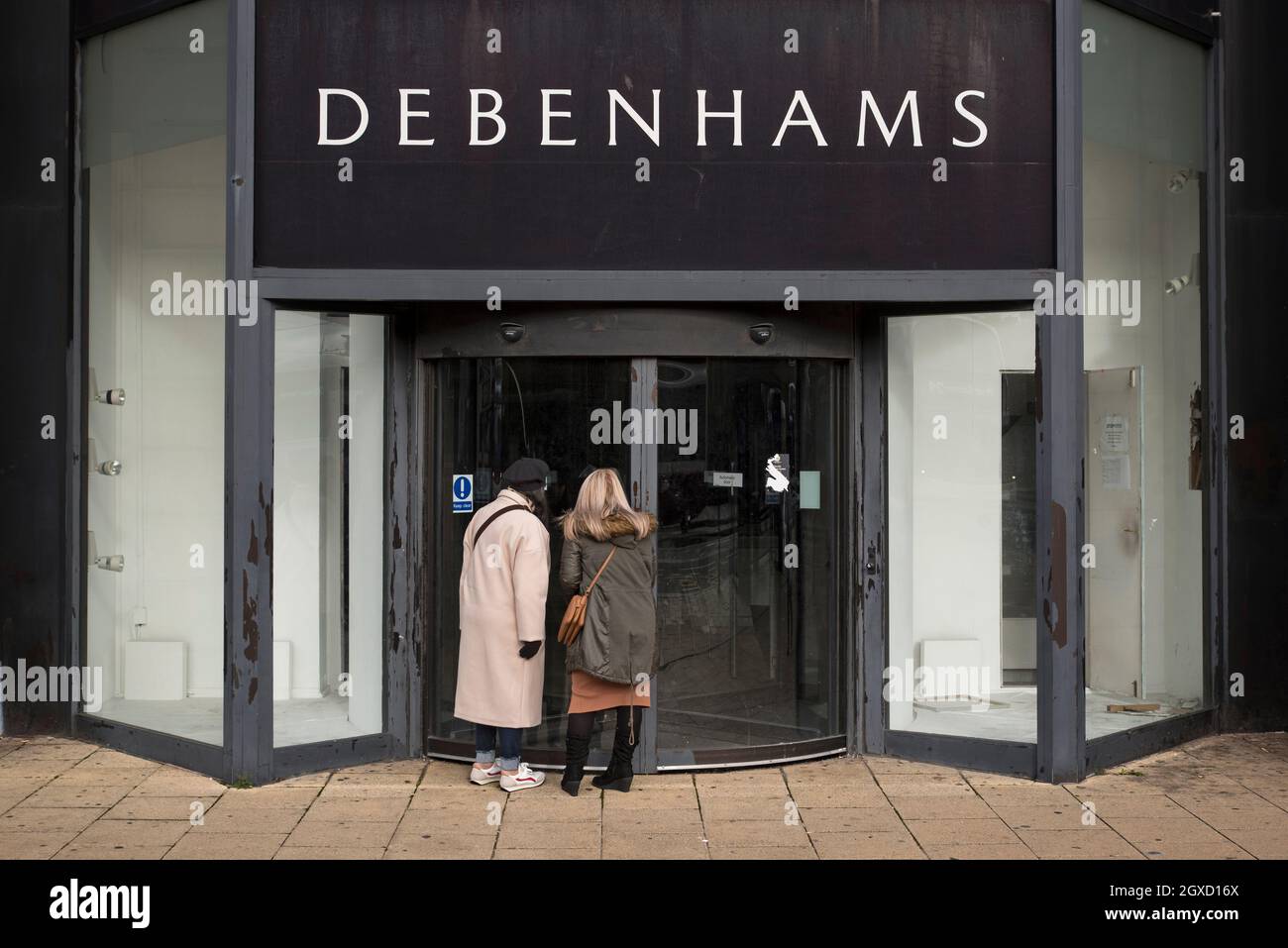 Two woman look in through the glass door of the closed and empty Debenhams store on Princes Street, Edinburgh, Scotland, Uk. Stock Photo
