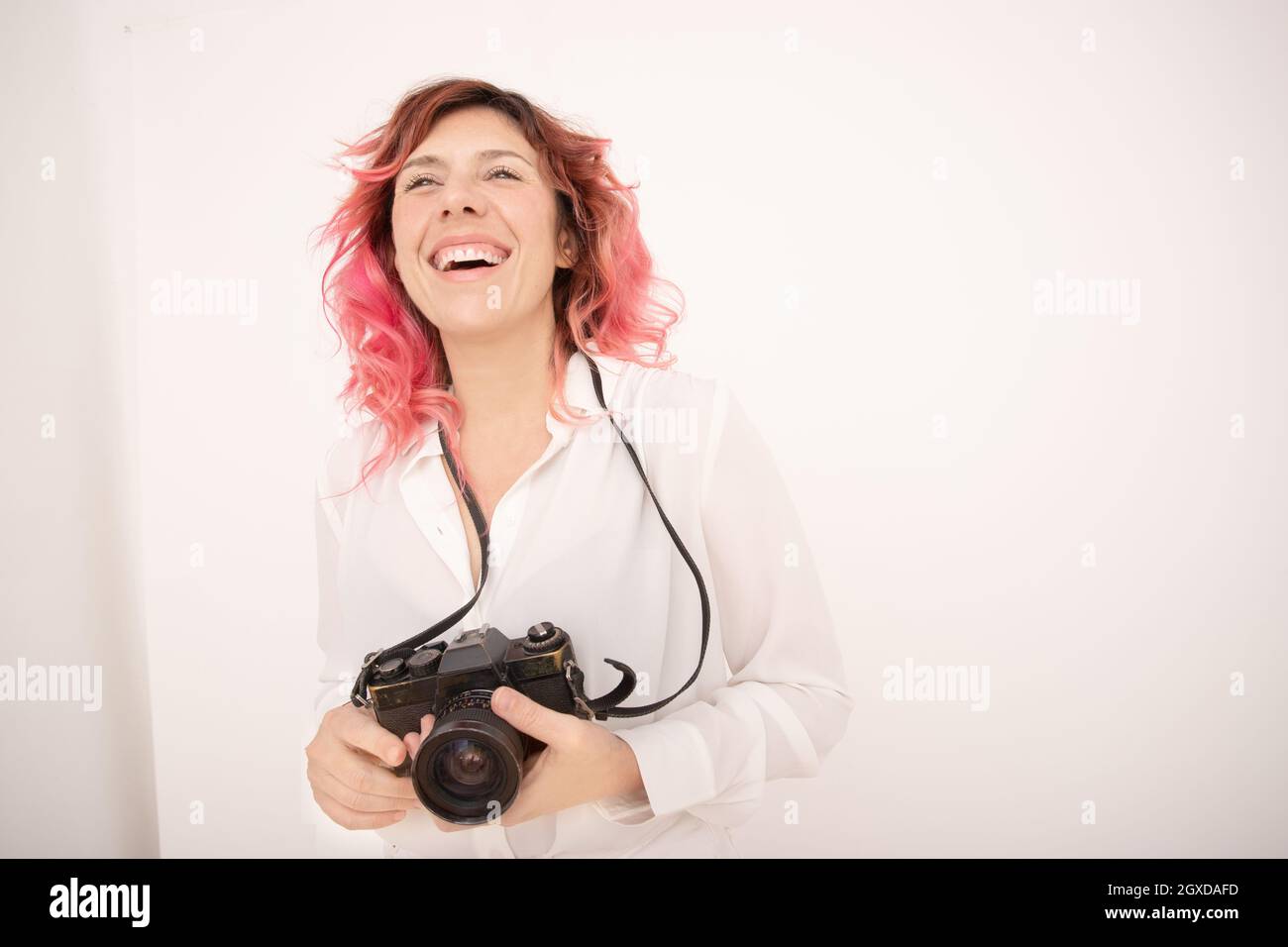 Smile female photographer with pink hair holding a professional photo camera in her hands in light room Stock Photo