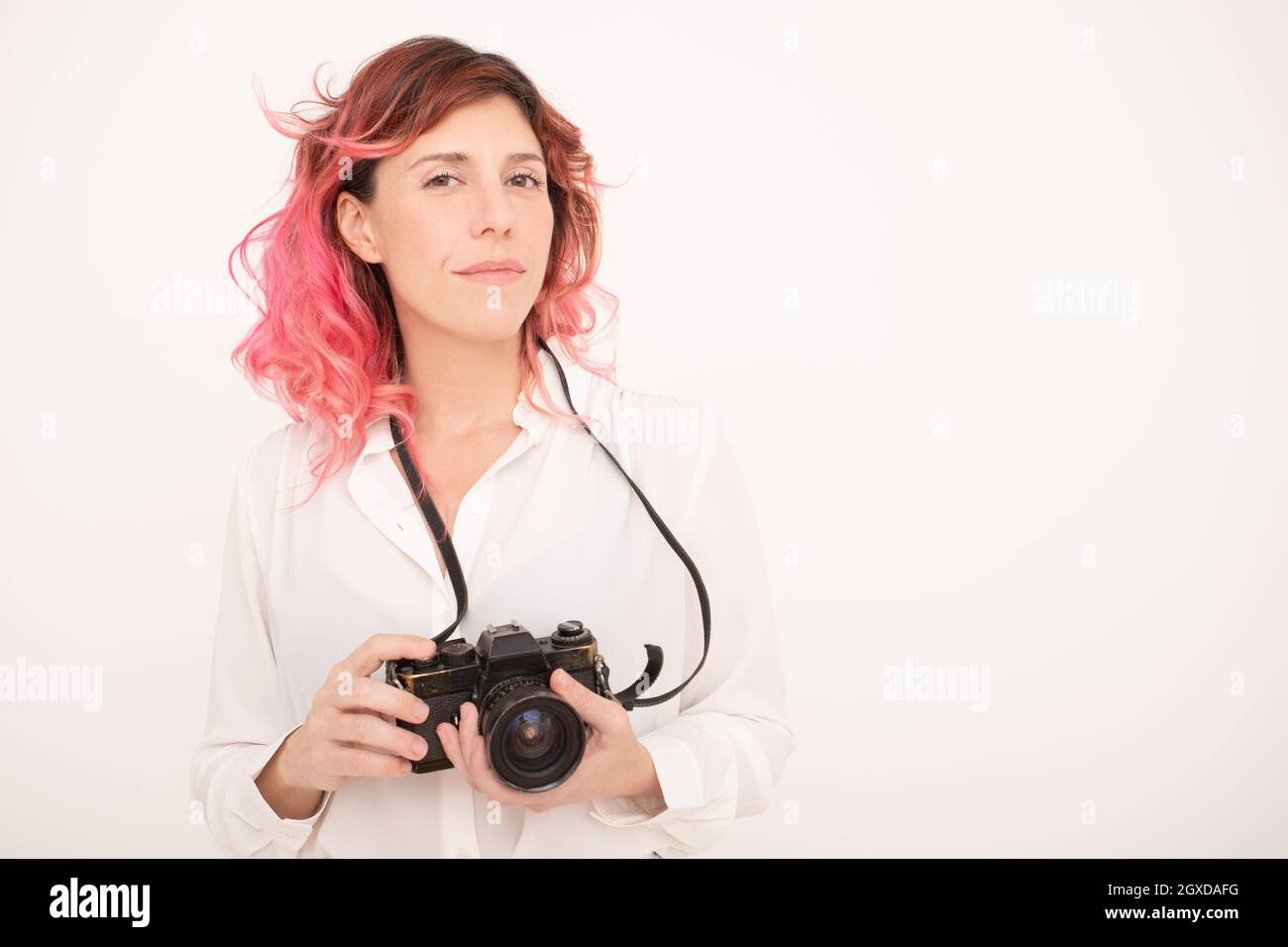 Pensive female photographer with pink hair holding a professional photo camera in her hands in light room Stock Photo
