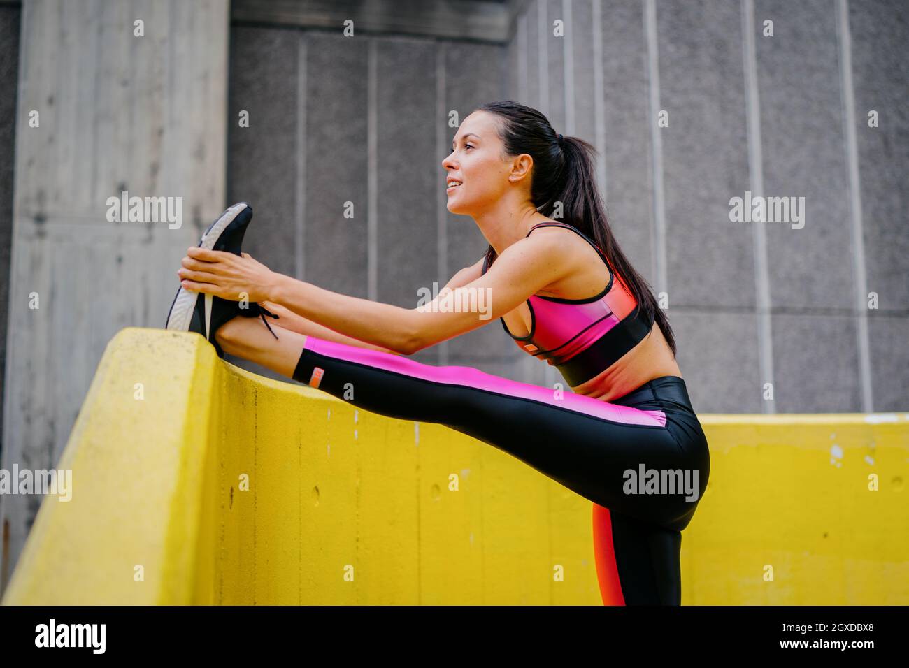 An athletic woman in a pink sports outfit stretching before a workout in an urban environment Stock Photo