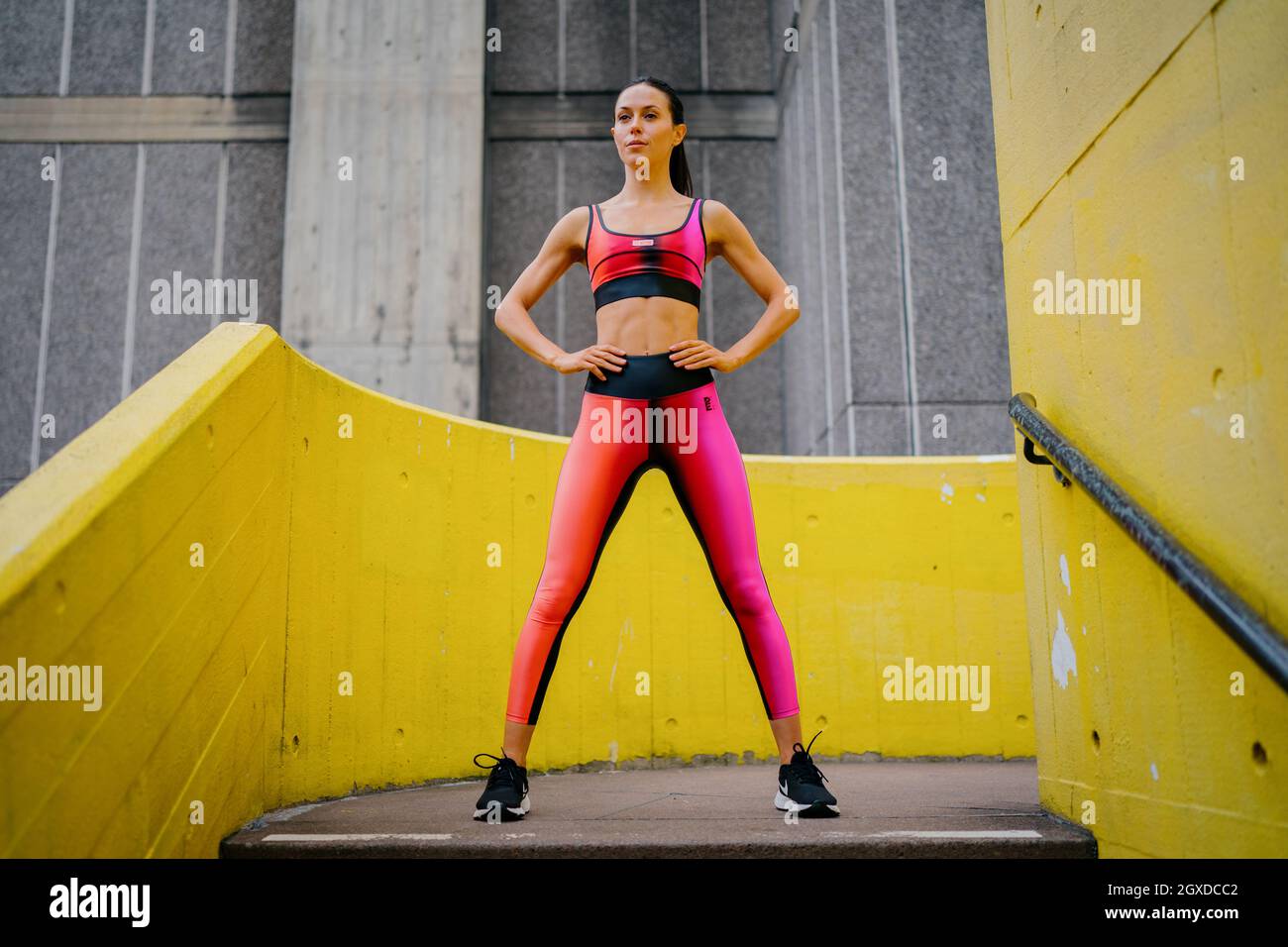 An athletic woman in a pink sports outfit poses in an urban environment Stock Photo
