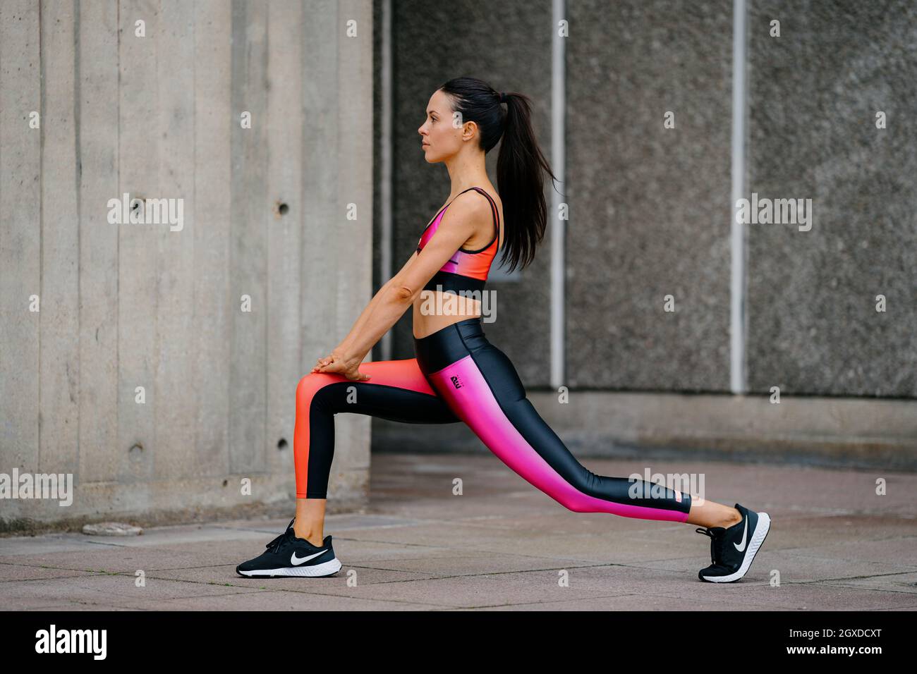 An athletic woman in a pink sports outfit stretching before a workout in an urban environment Stock Photo