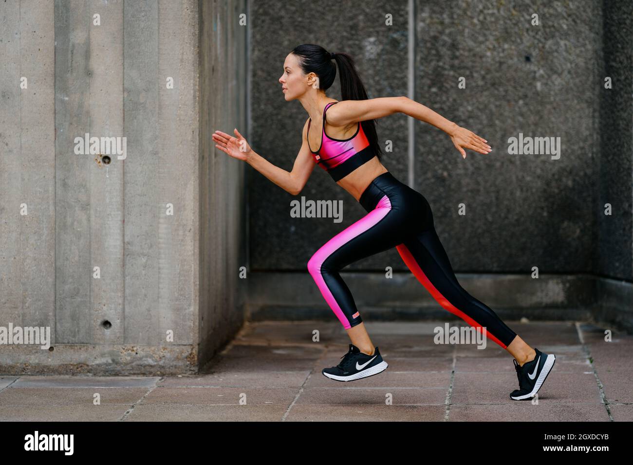 An athletic woman in a pink sports outfit running in an urban environment Stock Photo