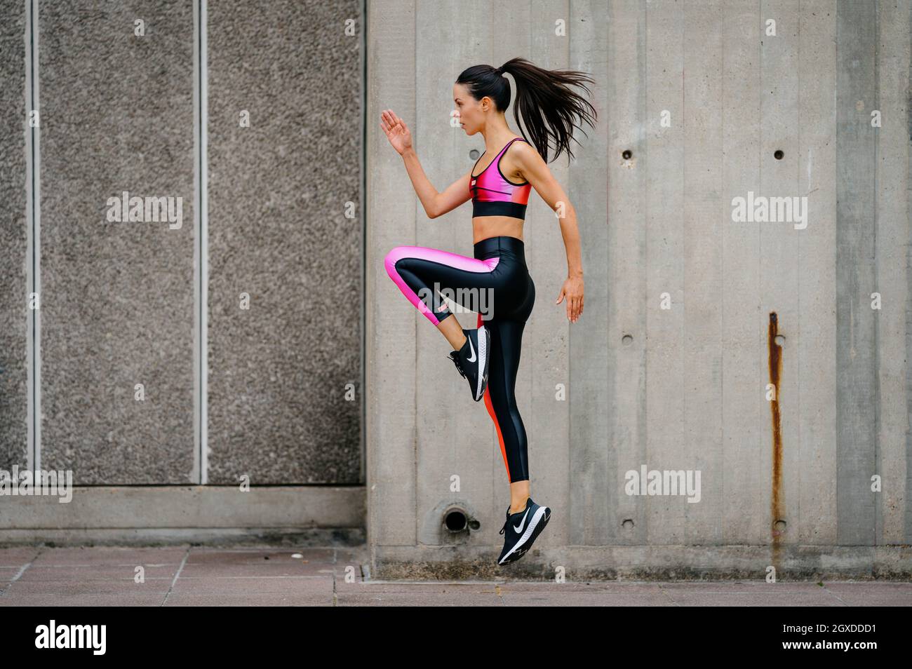 An athletic woman in a pink sports outfit jumping in an urban environment Stock Photo