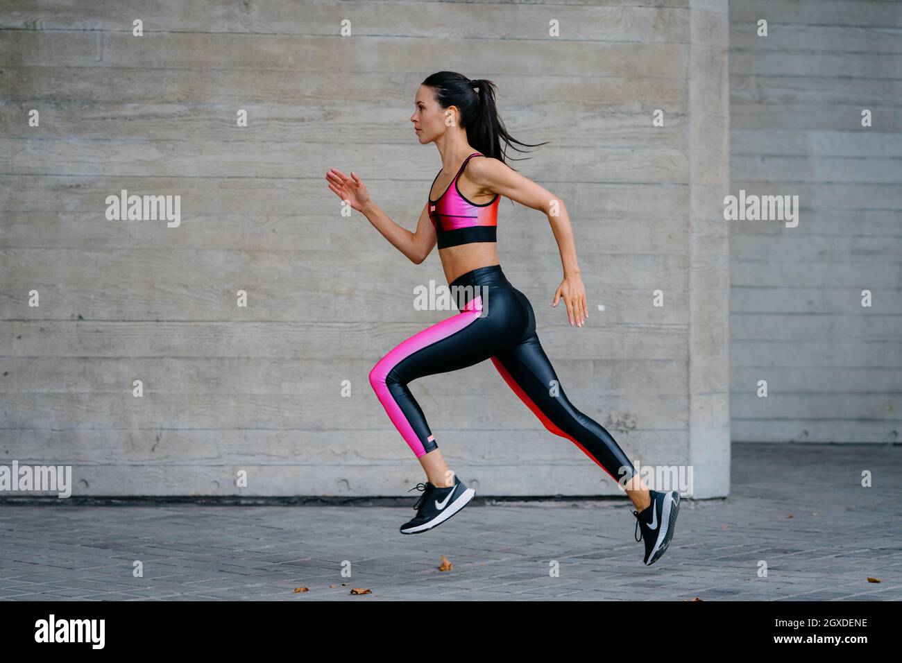 An athletic woman in a pink sports outfit running in an urban environment Stock Photo