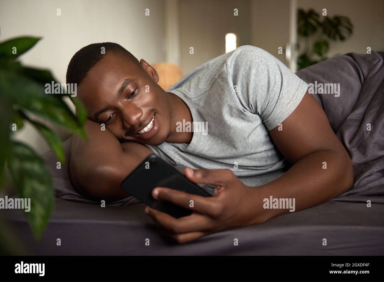 Smiling young African man texting in bed in the morning Stock Photo