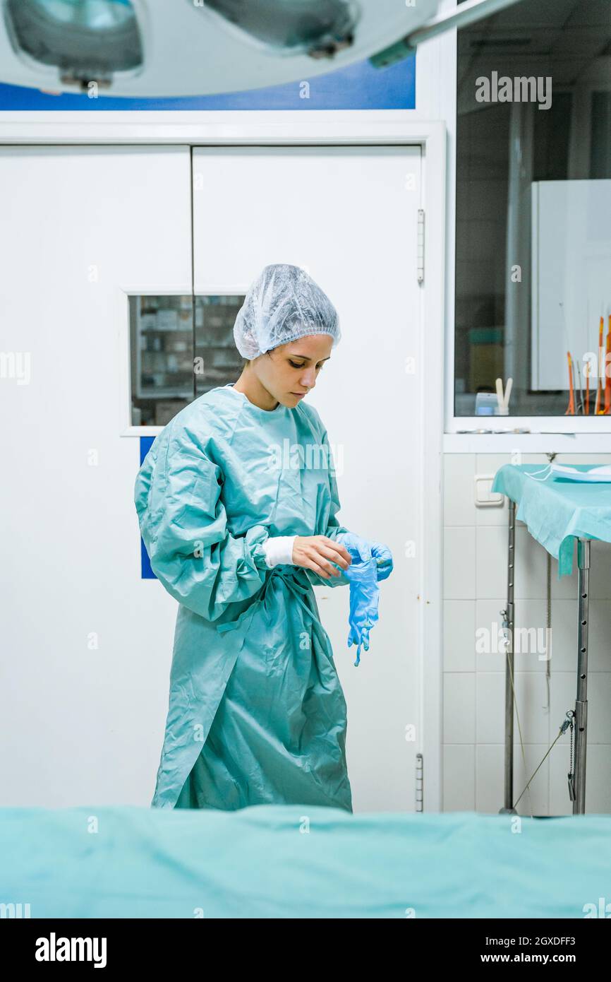 Young female veterinary surgeon in green uniform putting on sterile gloves in clinic Stock Photo