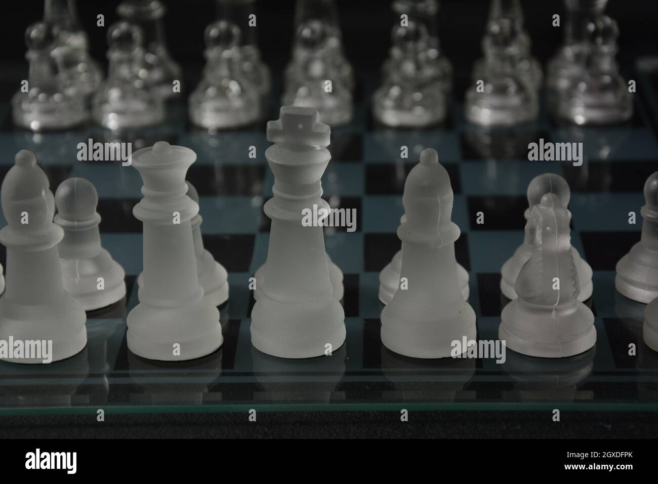 Clear glass chess pieces on a glass chessboard isolated on a black ...