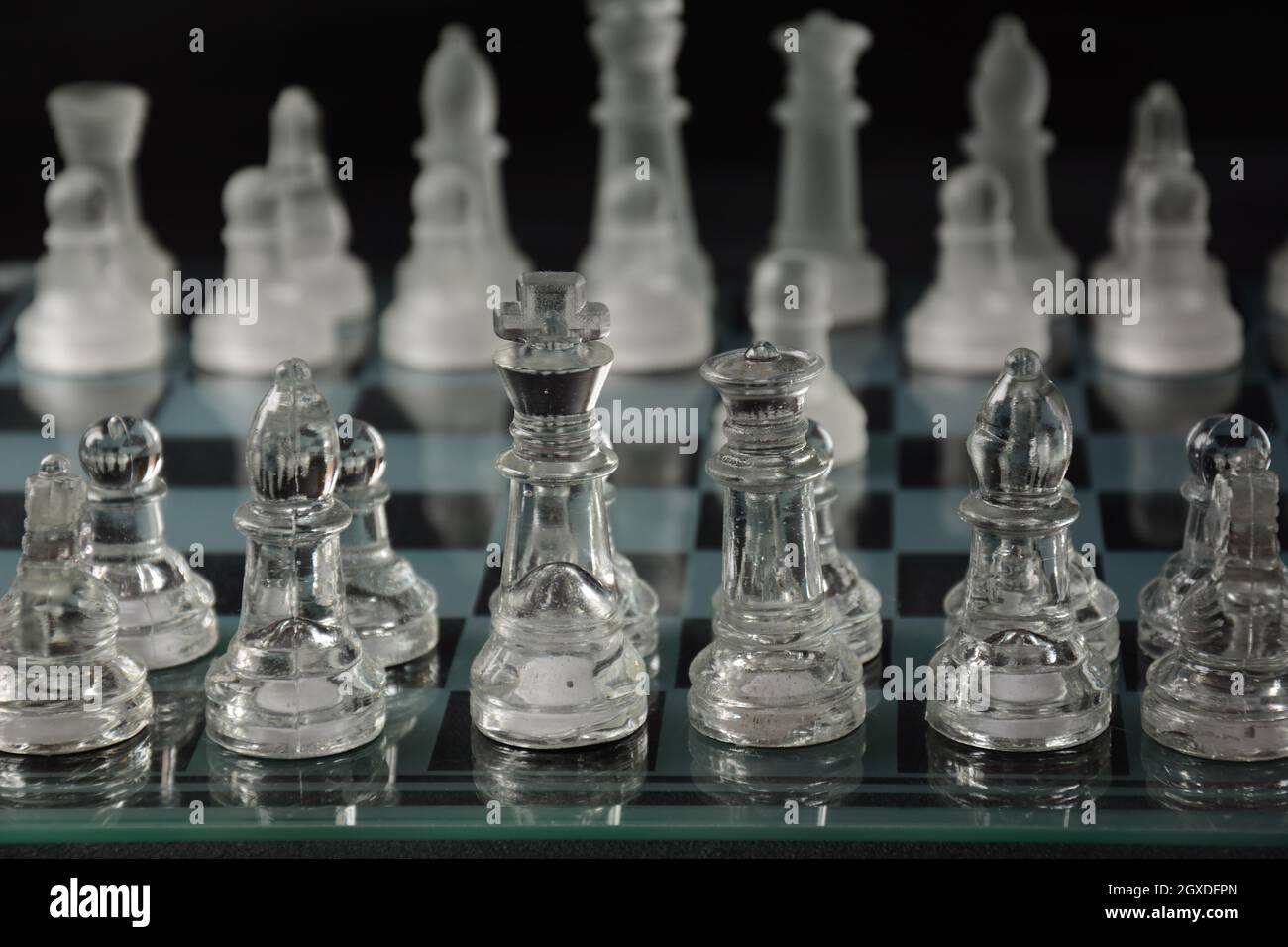 Clear glass chess pieces on a glass chessboard isolated on a black ...
