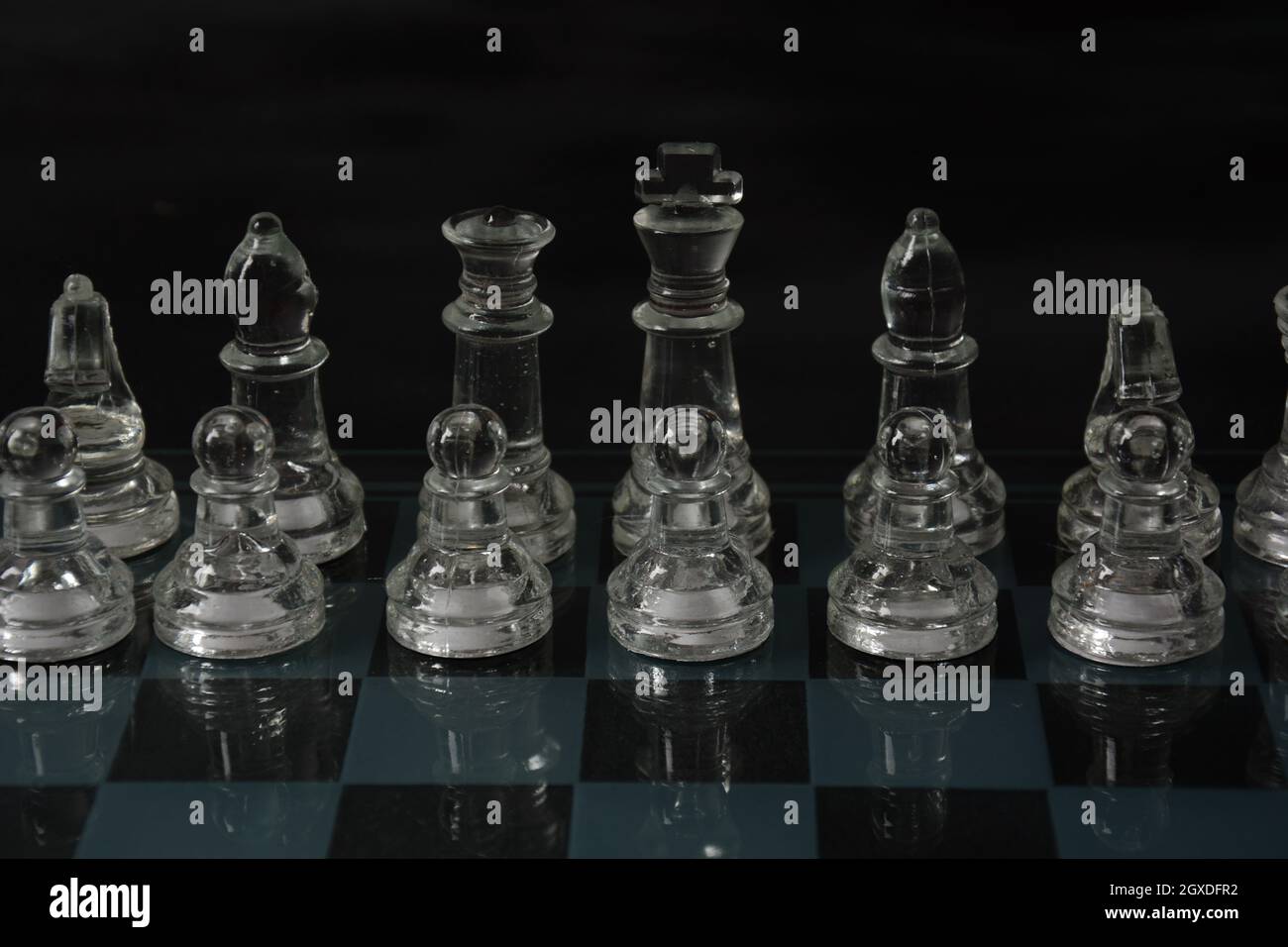 Clear glass chess pieces on a glass chessboard isolated on a black ...