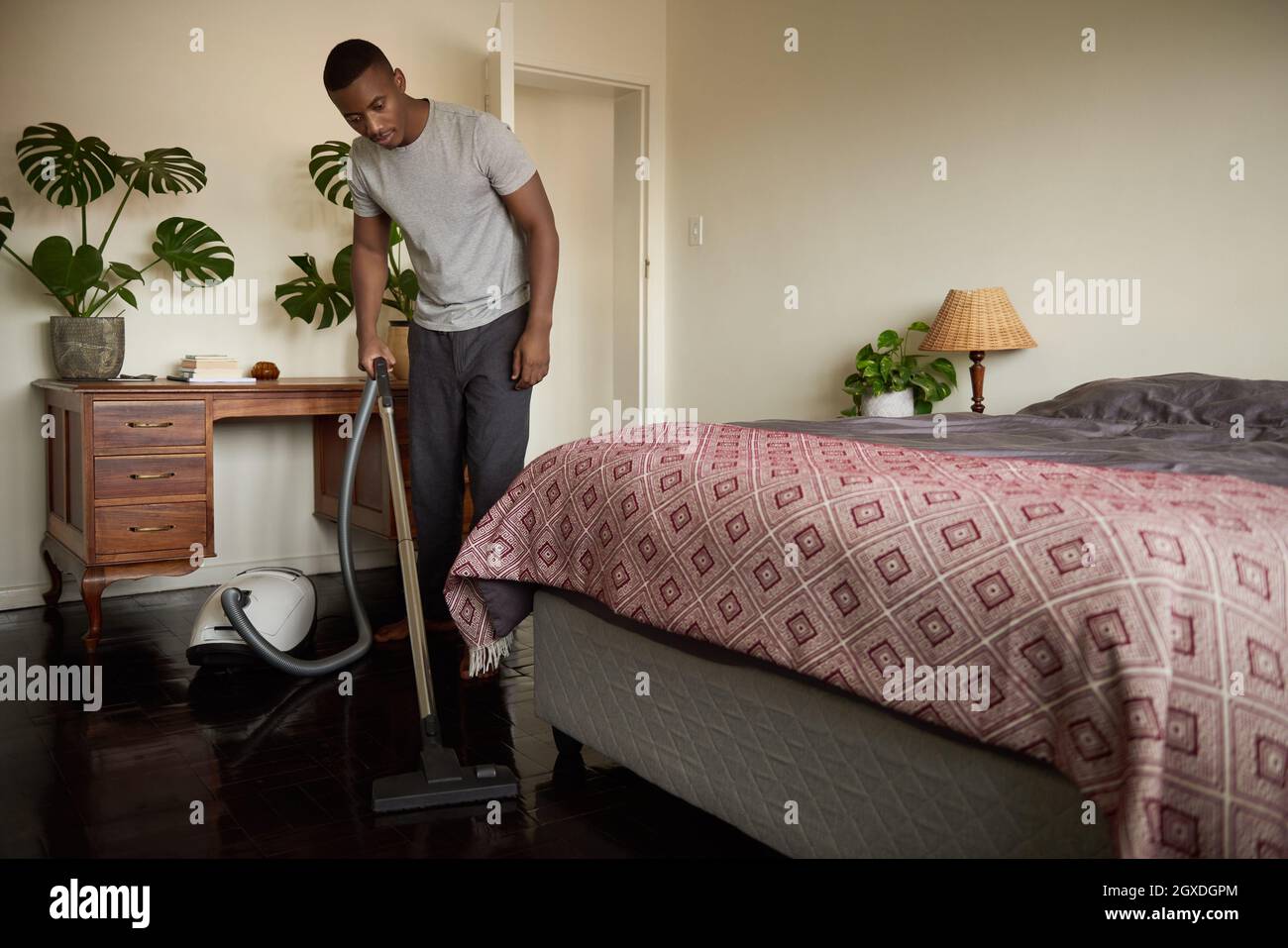 Young African man vacuuming his bedroom floor at home Stock Photo