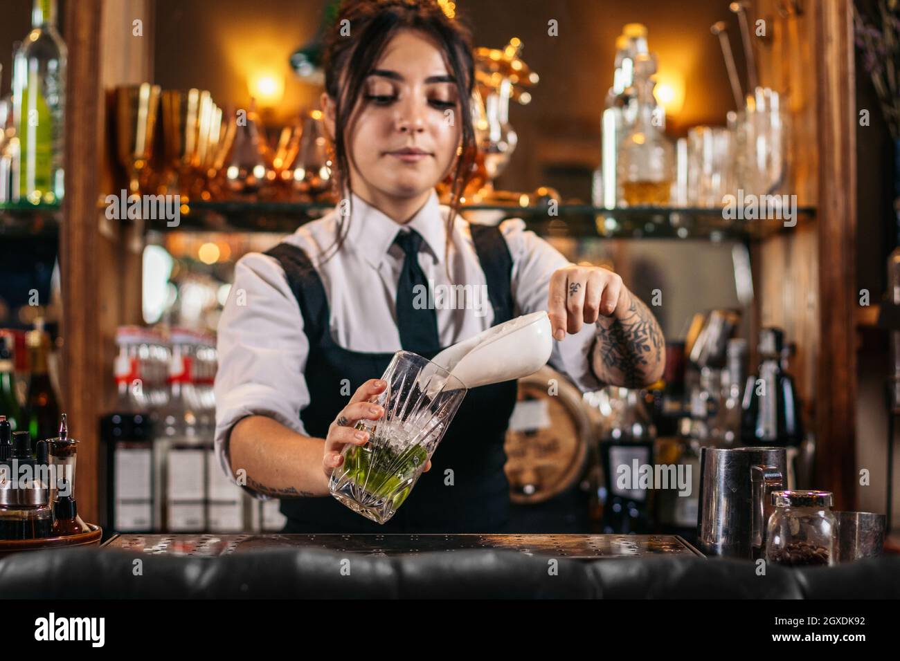 Concentrated female bartender in uniform pouring ice into glass while  working at counter in bar Stock Photo - Alamy
