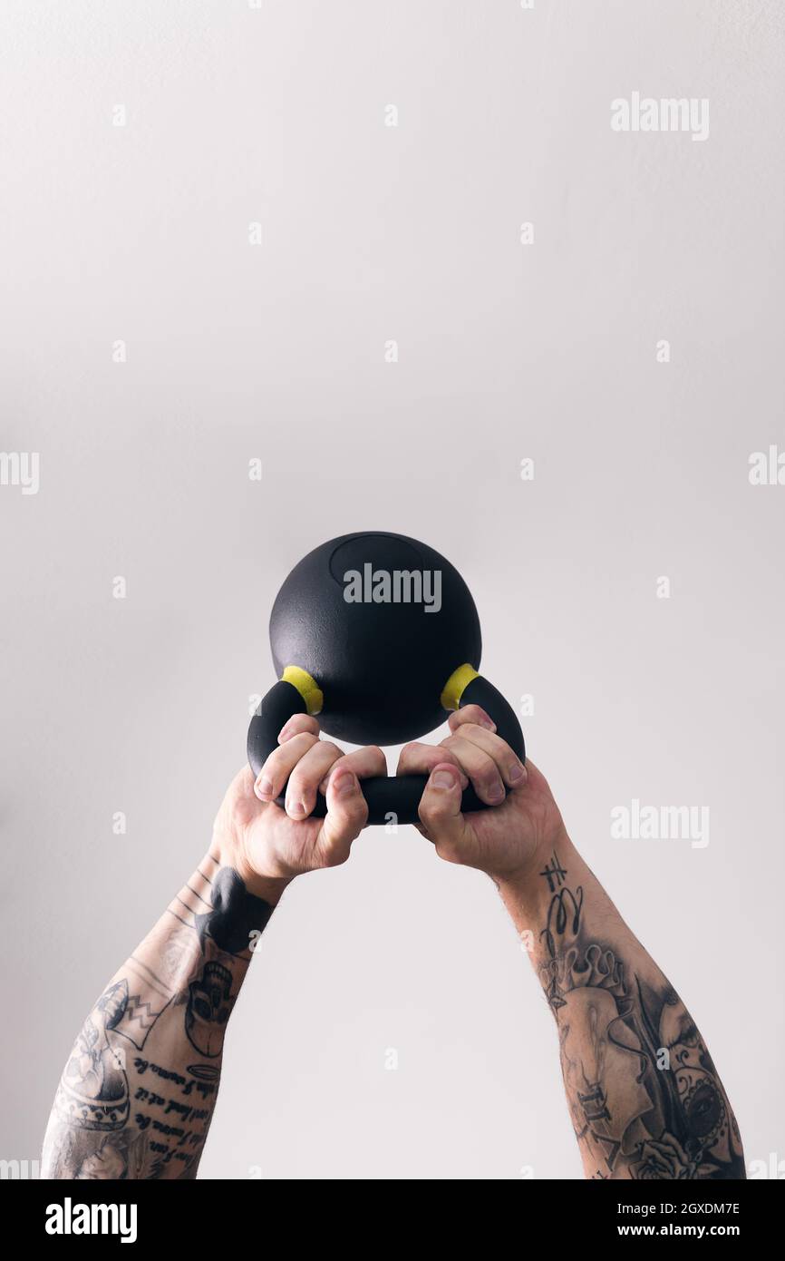 Concentrate strong man bodybuilder with tattoos lifting heavy kettlebell  white training in gym against light wall Stock Photo - Alamy