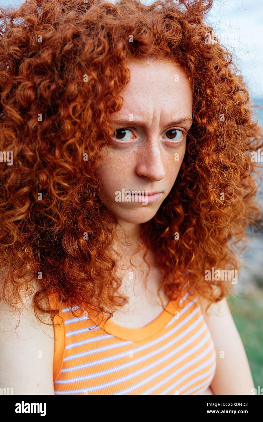 Upset female with curly ginger hair showing emotion of displease and looking at camera Stock Photo
