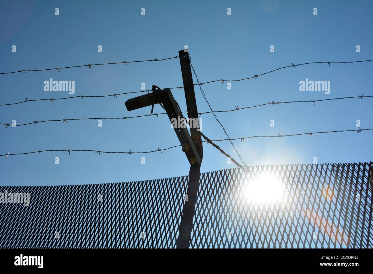 A metal fence with barbed wire , blue sky and sun Stock Photo - Alamy