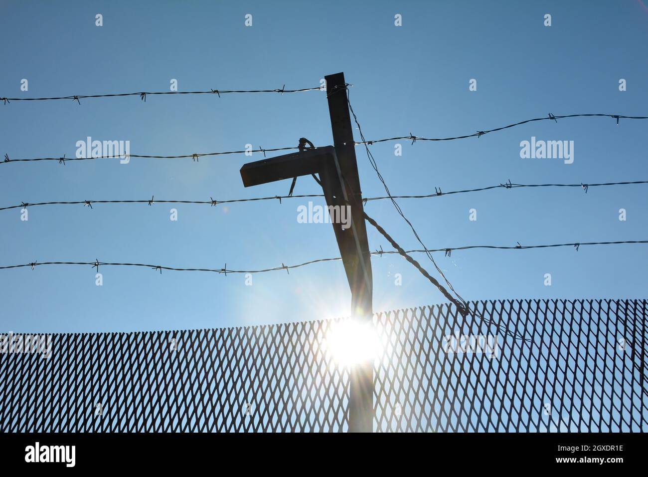 A metal fence with barbed wire , blue sky and sun Stock Photo - Alamy