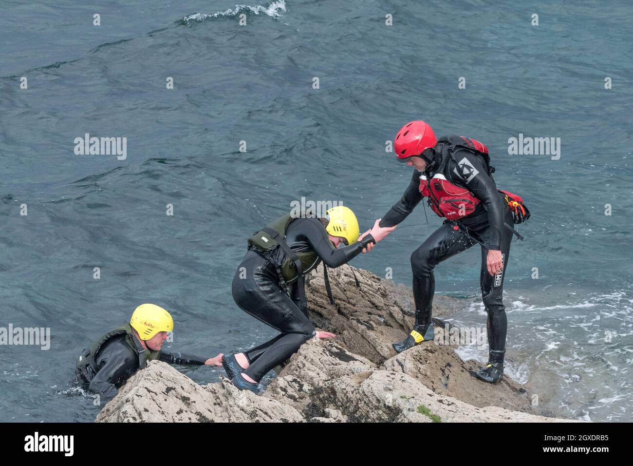 A coasteering instructor helping a holidaymaker out of the sea on a coasteering trip around Towan Head in Newquay in Cornwall. Stock Photo