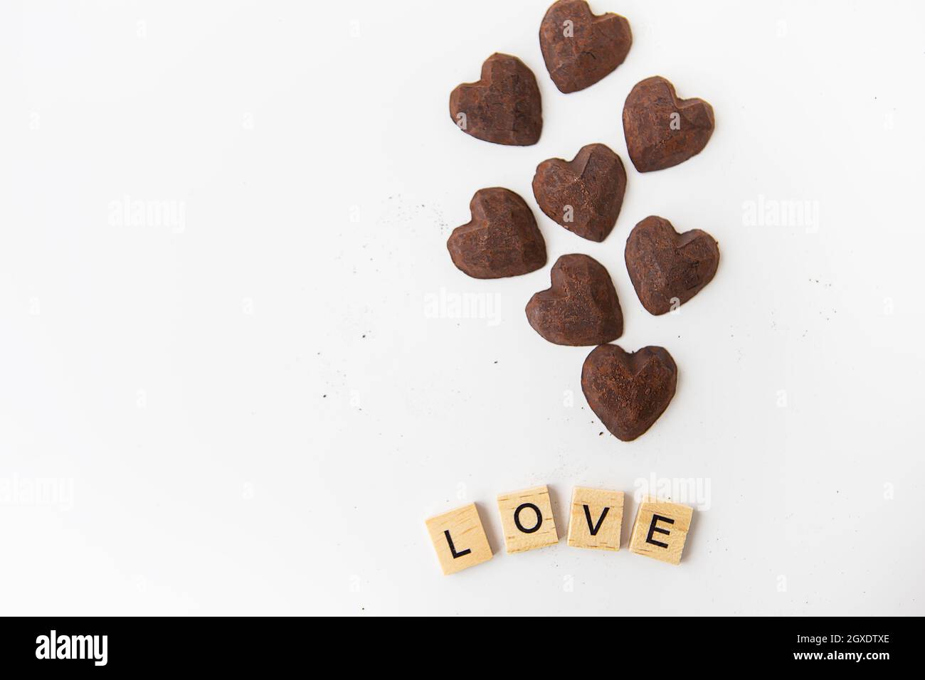 Truffle chocolate candies in the form of a heart on a white background. Inscription love made of wood letters. Place for an inscription Stock Photo