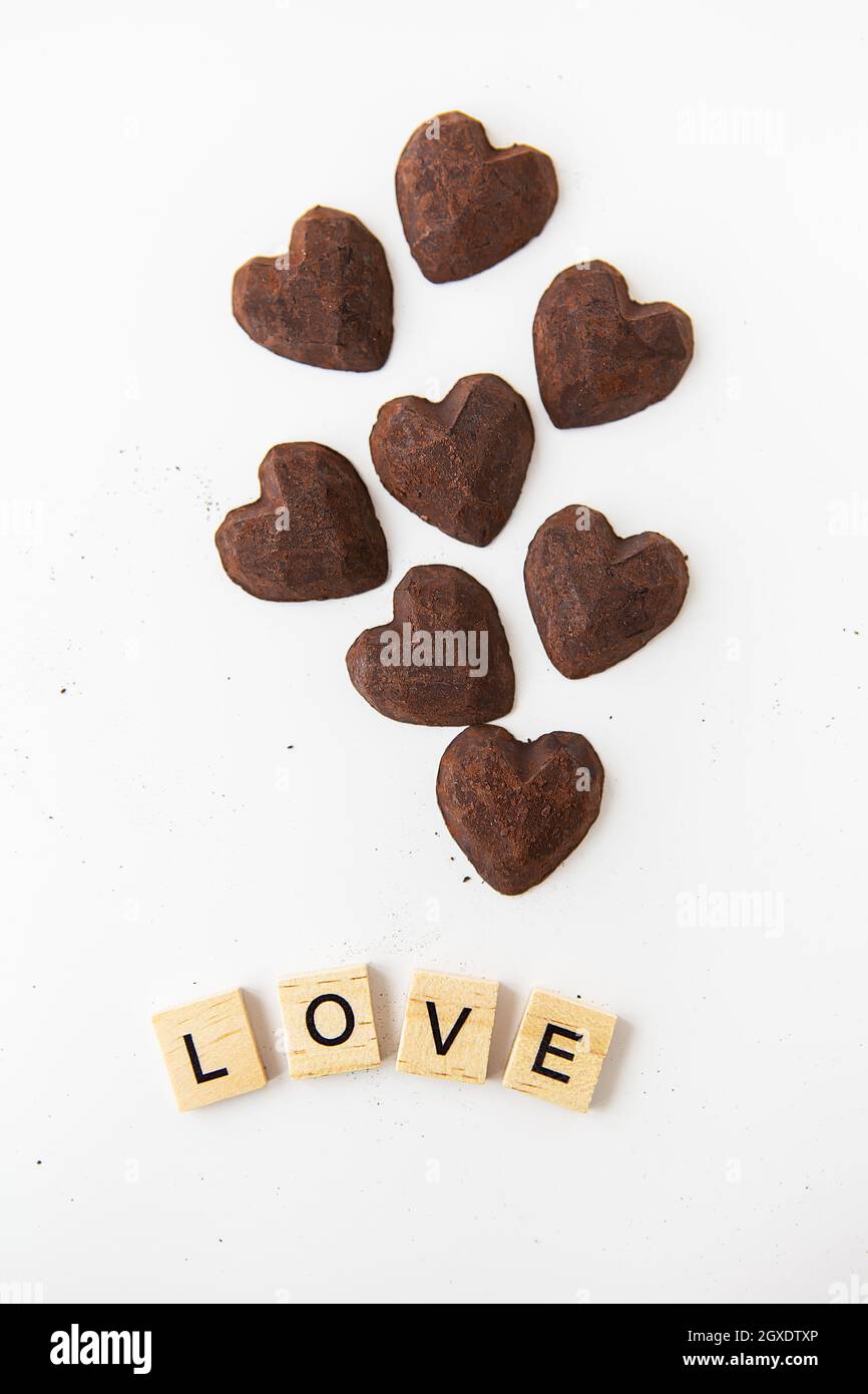 Truffle chocolate candies in the form of a heart on a white background. Inscription love made of wood letters Stock Photo