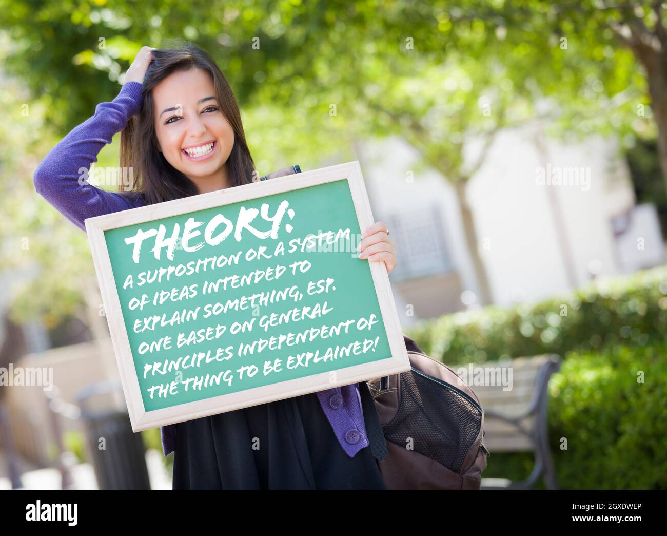 Excited Mixed Race Female Student Holding Chalkboard With Theory and the Definition Written on it. Stock Photo