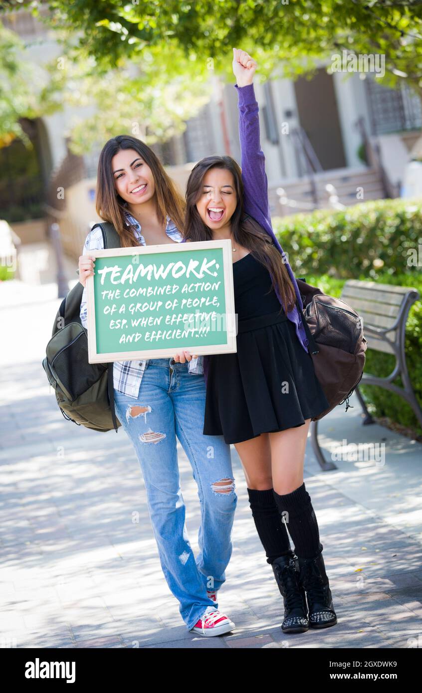 Excited Mixed Race Female Students Holding Chalkboard With Teamwork and the Definition Written on it. Stock Photo