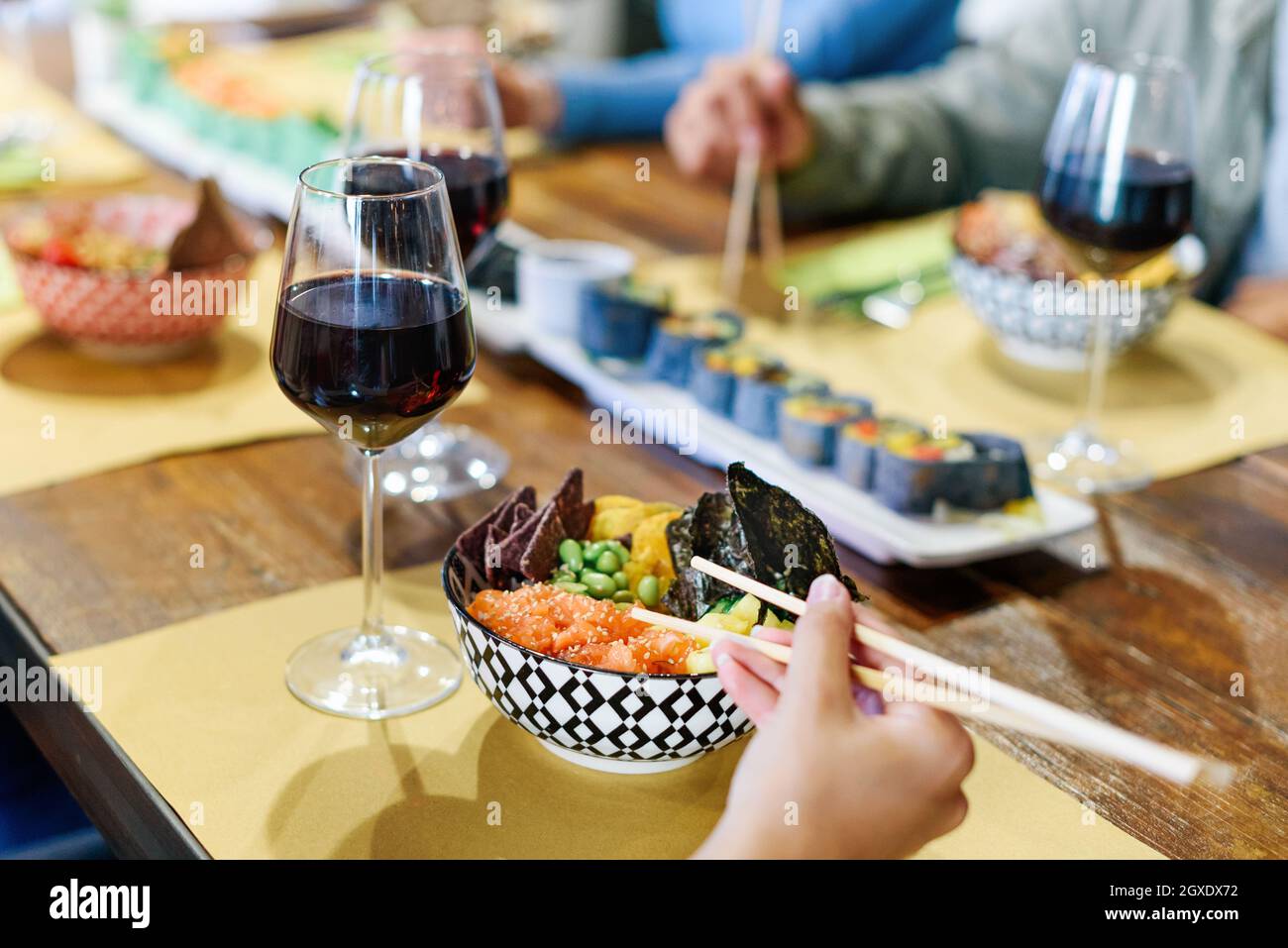 Person enjoying a bowl of poke or marinated seasoned raw fish with a glass of red wine in a restaurant with friends in a close up on the food Stock Photo