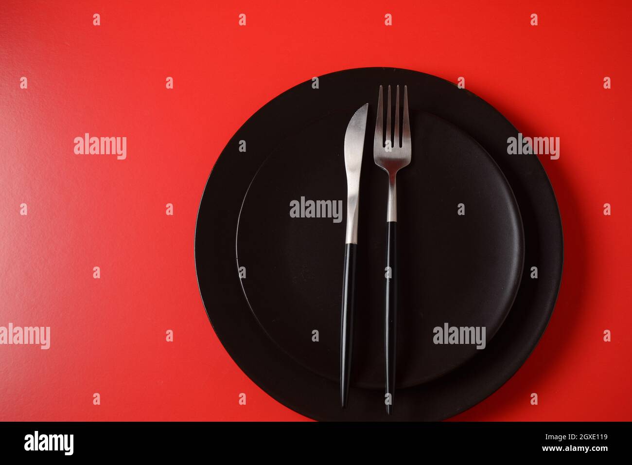 Black plate, cutlery on red background. Setting up a table Stock Photo