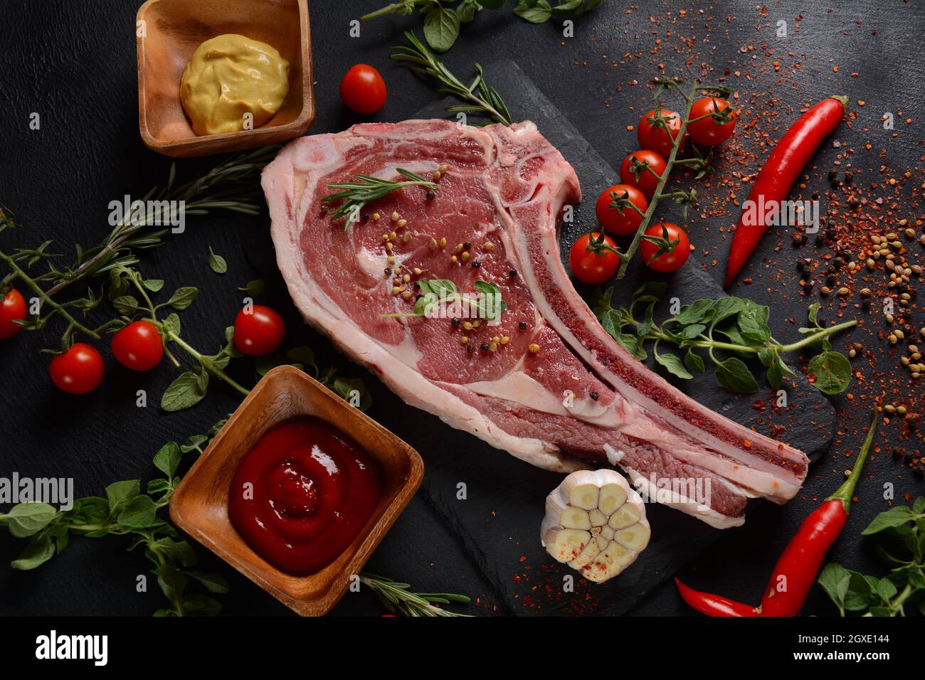 Fresh Raw Beef bone rib steak on black board with herbs and spices