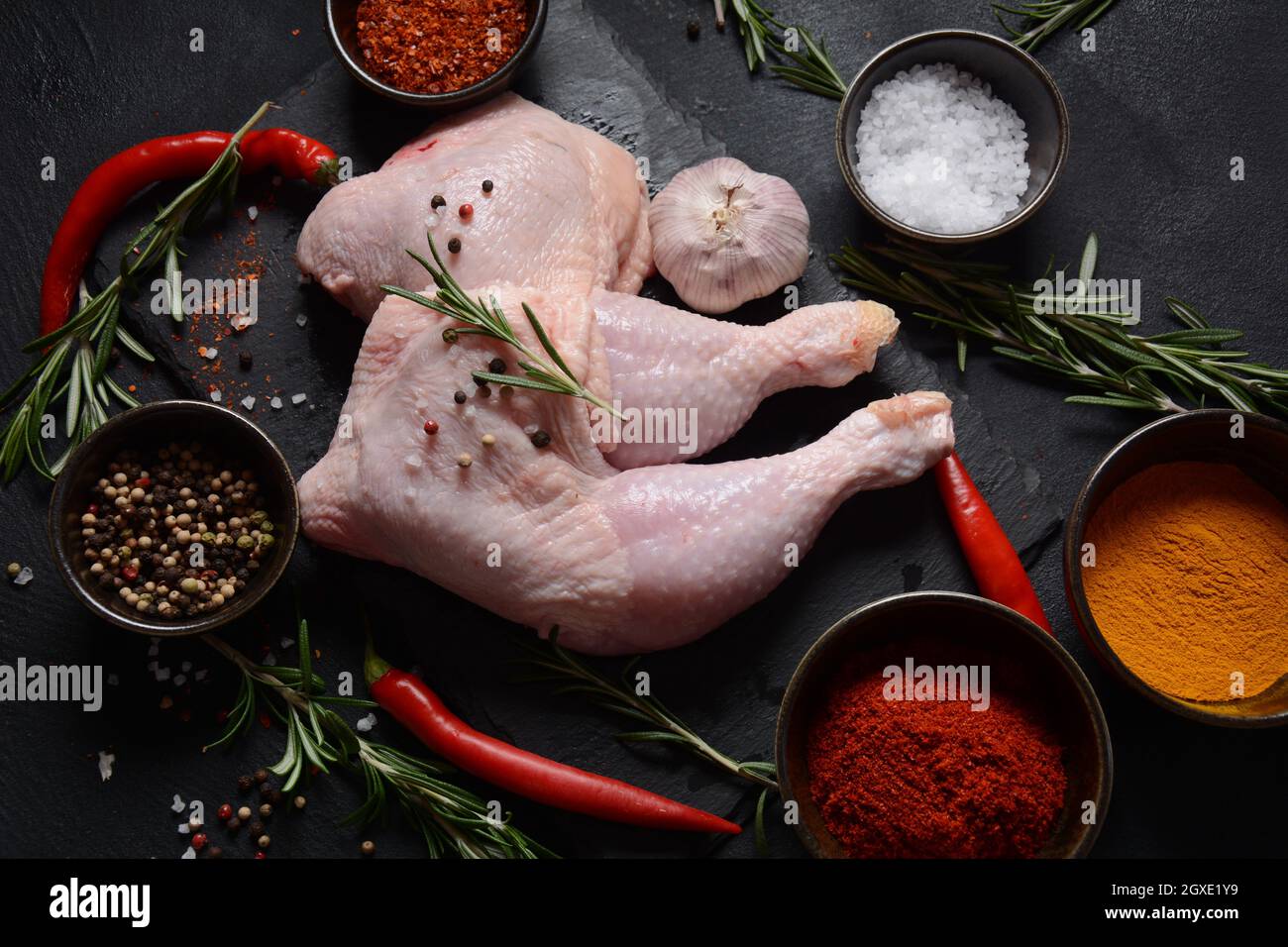 Raw chicken quarters, legs with herbs and spices ready for grill on a dark background. Stock Photo