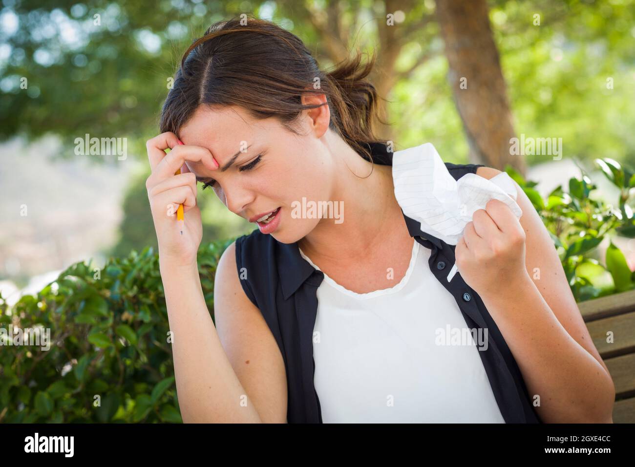 Frustrated and Upset Young Woman with Pencil and Crumpled Paper in Her Hand Sitting on Bench Outside. Stock Photo