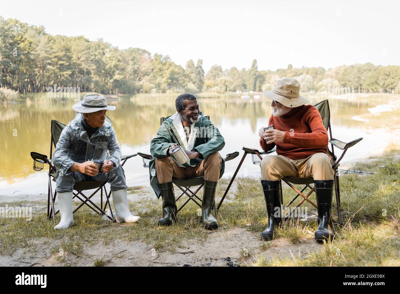 Cheerful multicultural men in fishing outfit holding thermo cups near lake  Stock Photo - Alamy
