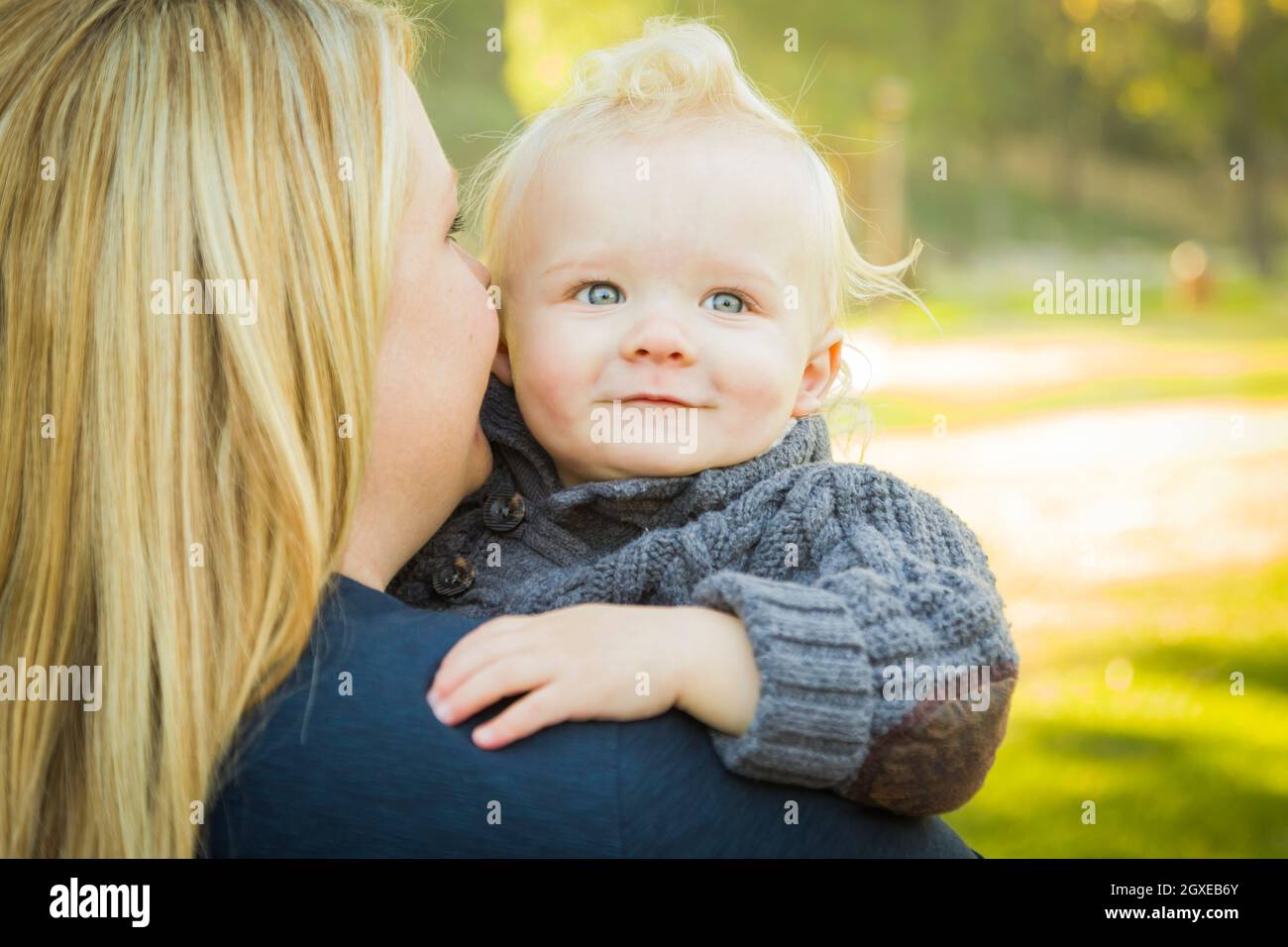 Mother Embracing Her Adorable Blonde Haired Blue Eyed Baby Boy Outdoors. Stock Photo