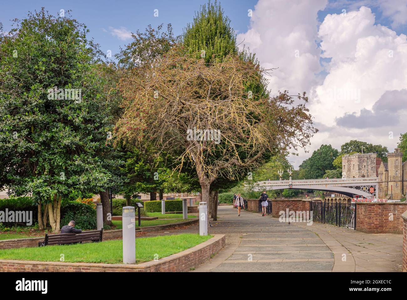 A path thorough a park runs alongside a river with a historic bridge in ...