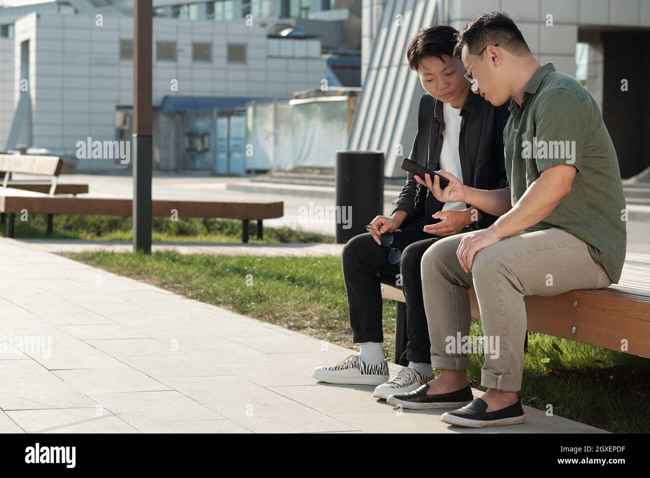 Two young Chinese businessmen looking through data on smartphone screen Stock Photo