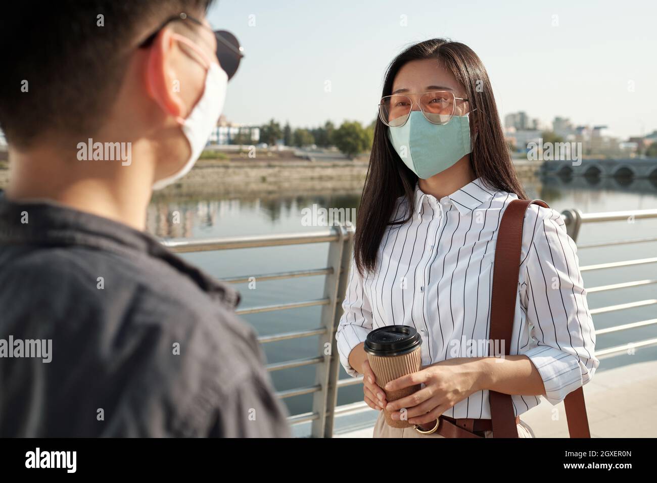 Young Asian female in eyeglasses and protective mask talking to colleague Stock Photo