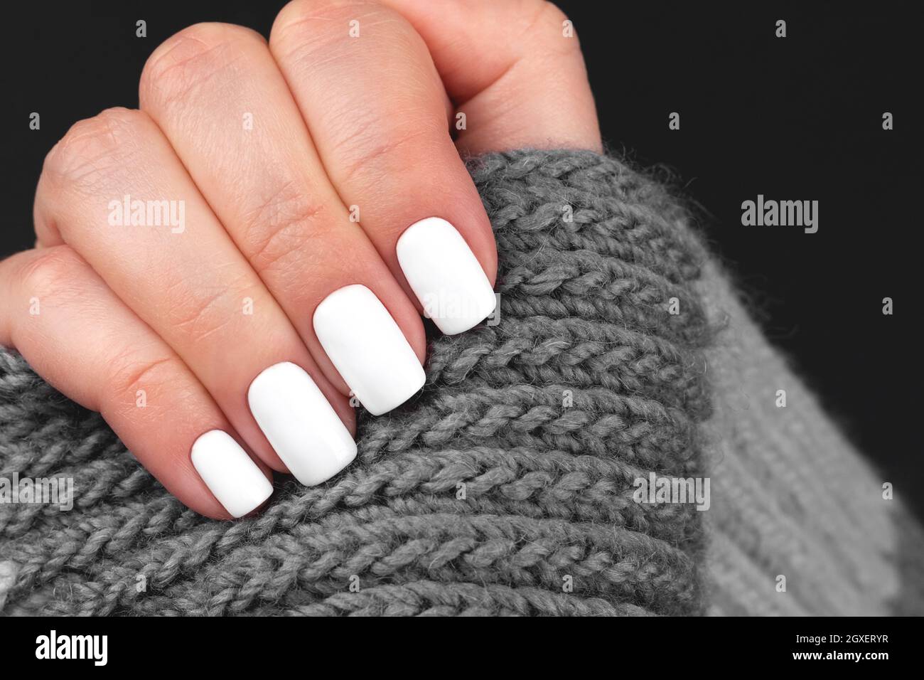 Female hand with gray knitted scarf with beautiful manicure - white nails. Nail care concept Stock Photo