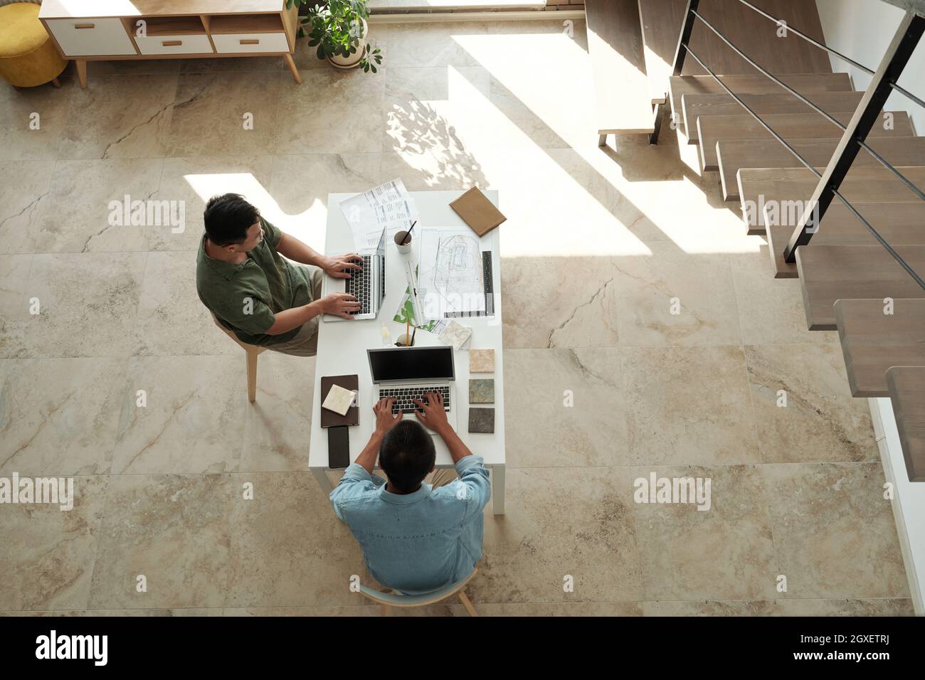 Two young designers or architects typing on laptops while sitting by table in office Stock Photo