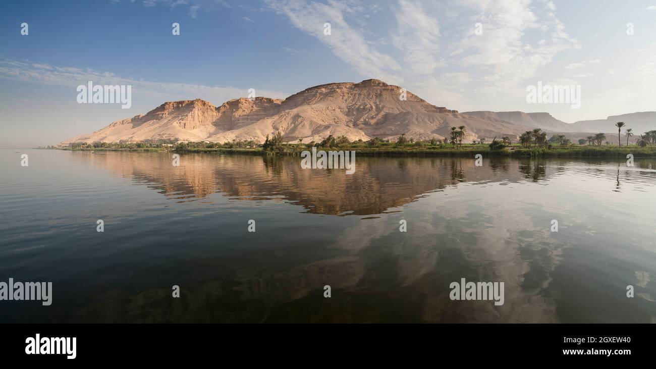 Distant desert mountain panorama with fertile green area in front reflected in the very clam water of the river Nile, Egypt Stock Photo