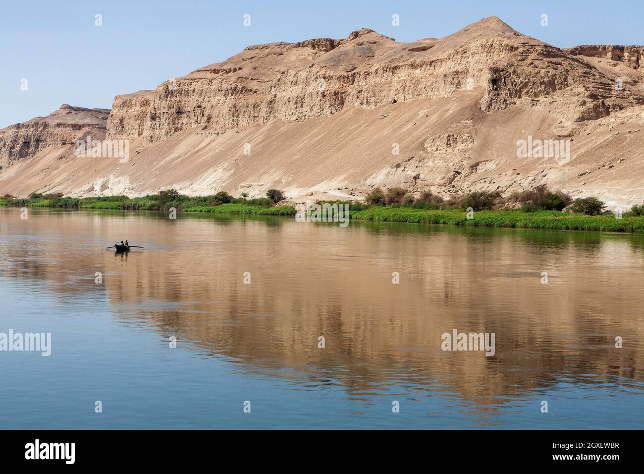 Two fishermen in a small boat on the Nile very small in the vast reflection of the desert mountains behind Stock Photo