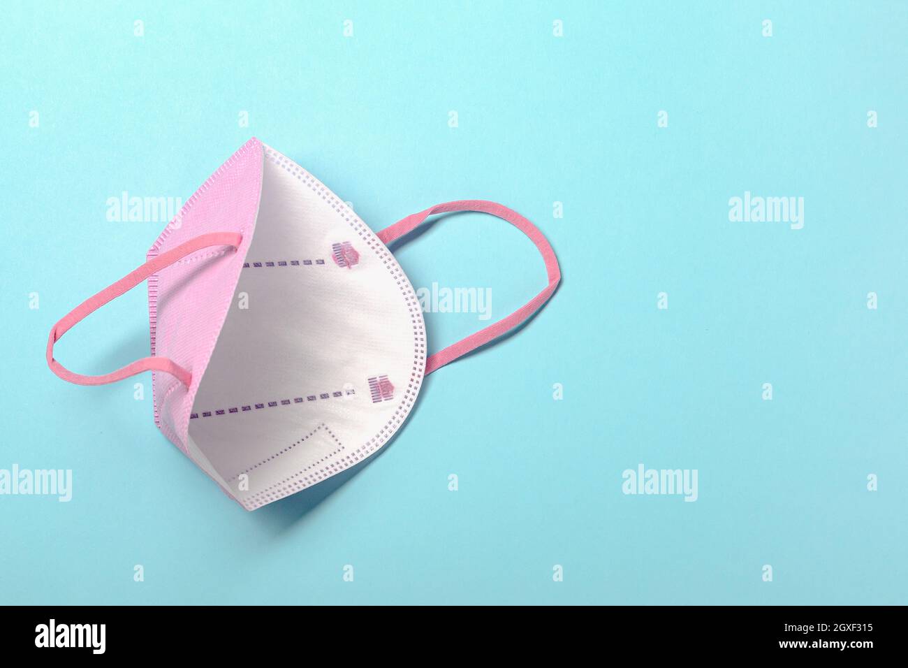 Pink KN95 or N95 FFP2 mask for protection and corona virus on pastel blue background. Anti pollution concept. copy space, from above. Stock Photo