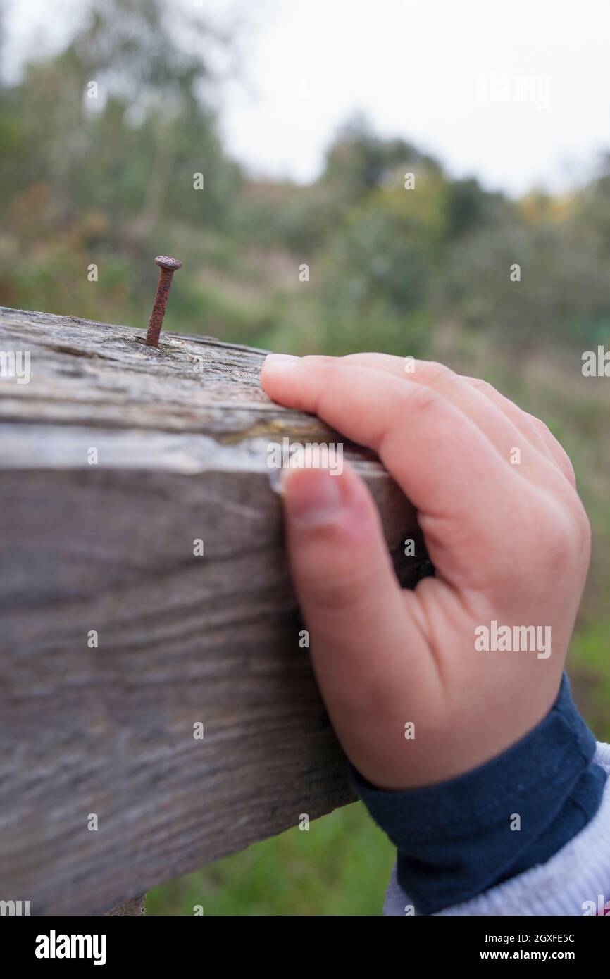 Child boy hand grabbing a board with rusty nail near. Selective focus Stock Photo