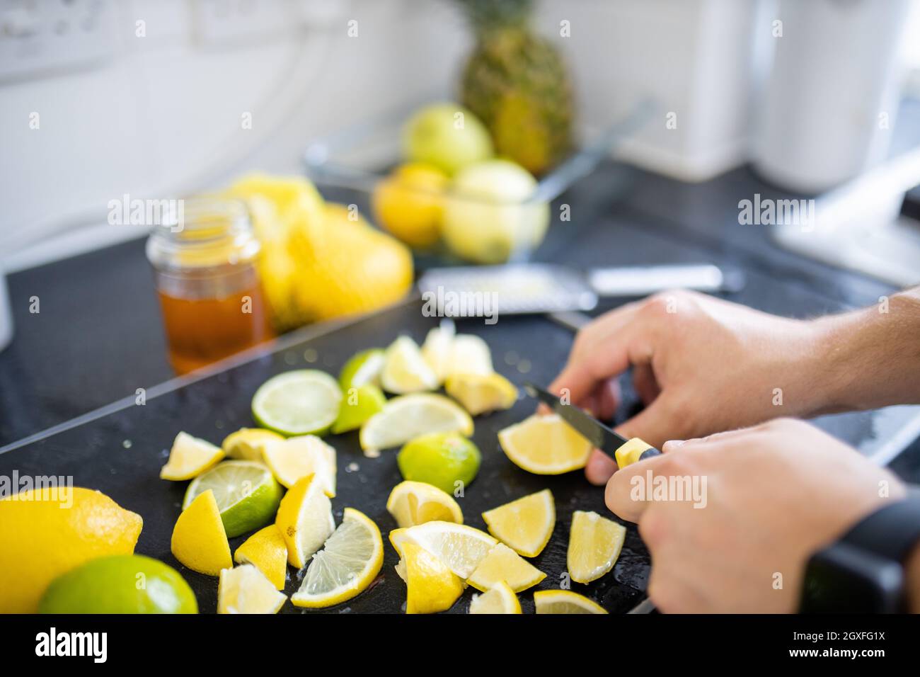 Male hands carefully slicing lemons and limes above black tray. Man cutting lemons into small pieces on a tray. Citrus drink preparation Stock Photo